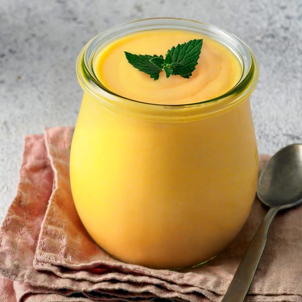 A glass jar of Mawa House's yellow mango lassi, garnished with fresh mint leaves.