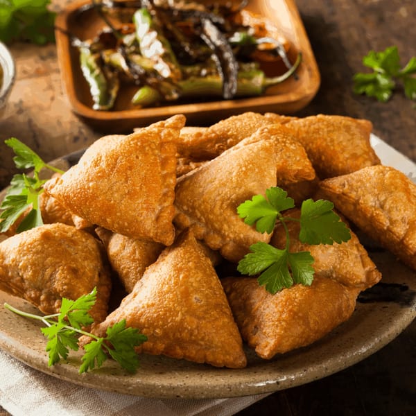 A plate of golden-brown Mawa House samosas garnished with fresh parsley, alongside a dish of roasted peppers.