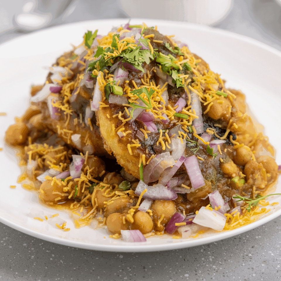 A plate of Mawa House's Indian chaat, topped with chickpeas, onions, cilantro, and crispy noodles.